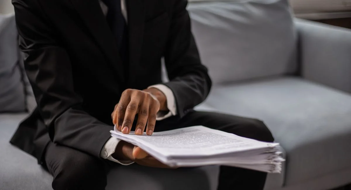 Close-up of a businessman in a suit reviewing documents while seated on a sofa indoors.