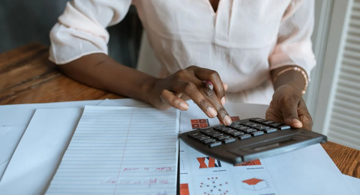 A professional woman calculating finances at a desk with charts and a calculator.