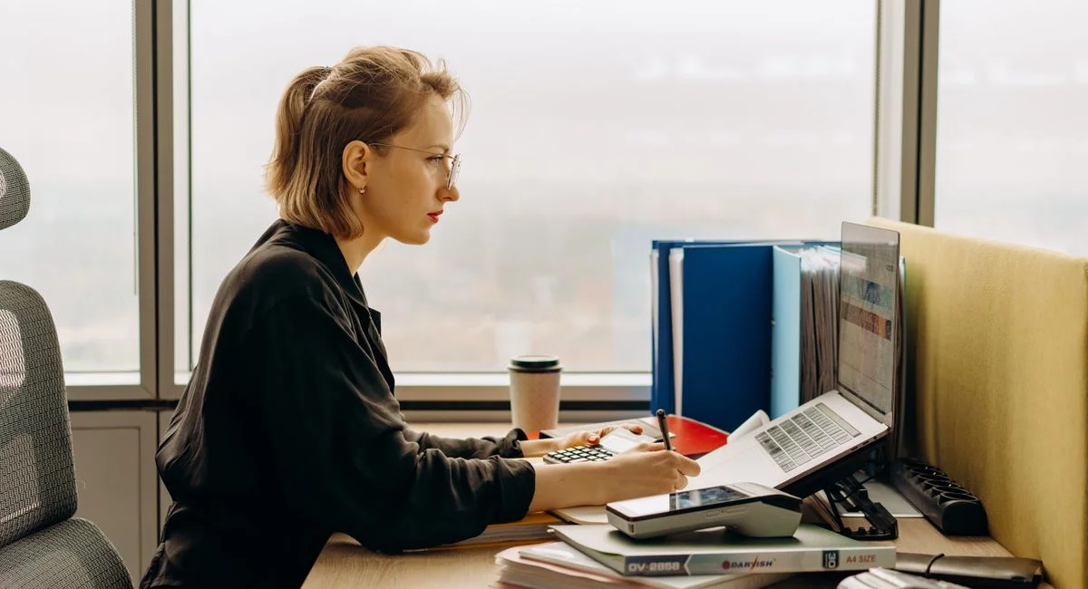 Dedicated woman using laptop and calculator in modern office setting.