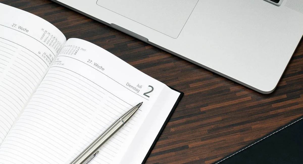 Open planner with a pen and laptop on a wooden desk, ready for organization.