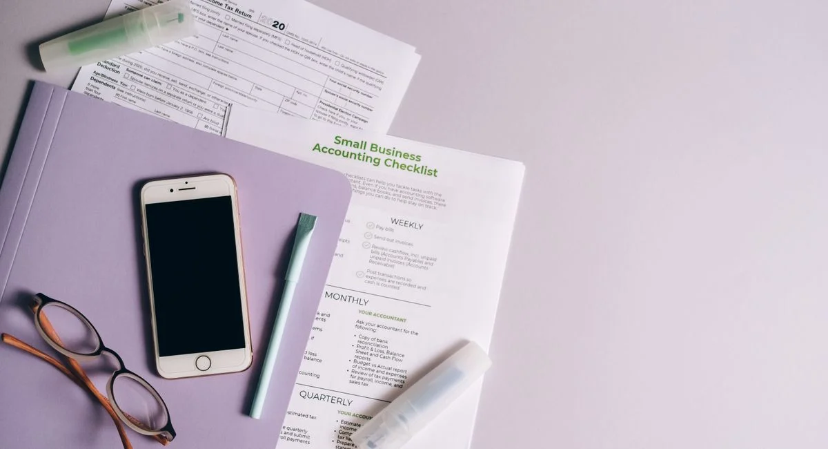 Flat lay of accounting documents, smartphone, and glasses on a desk.