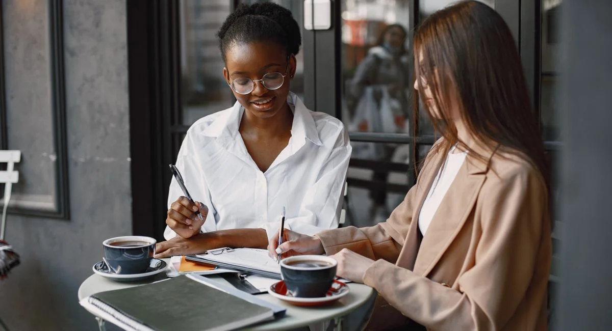 Two professional women engaged in a collaborative meeting at an outdoor cafe table.