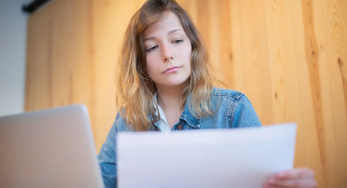 Businesswoman in a denim jacket analyzing documents at a wooden table in a cozy workspace.