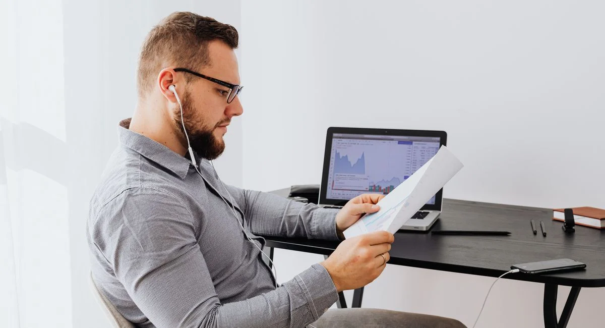 Professional analyzing financial charts on laptop and paperwork in an office setting.