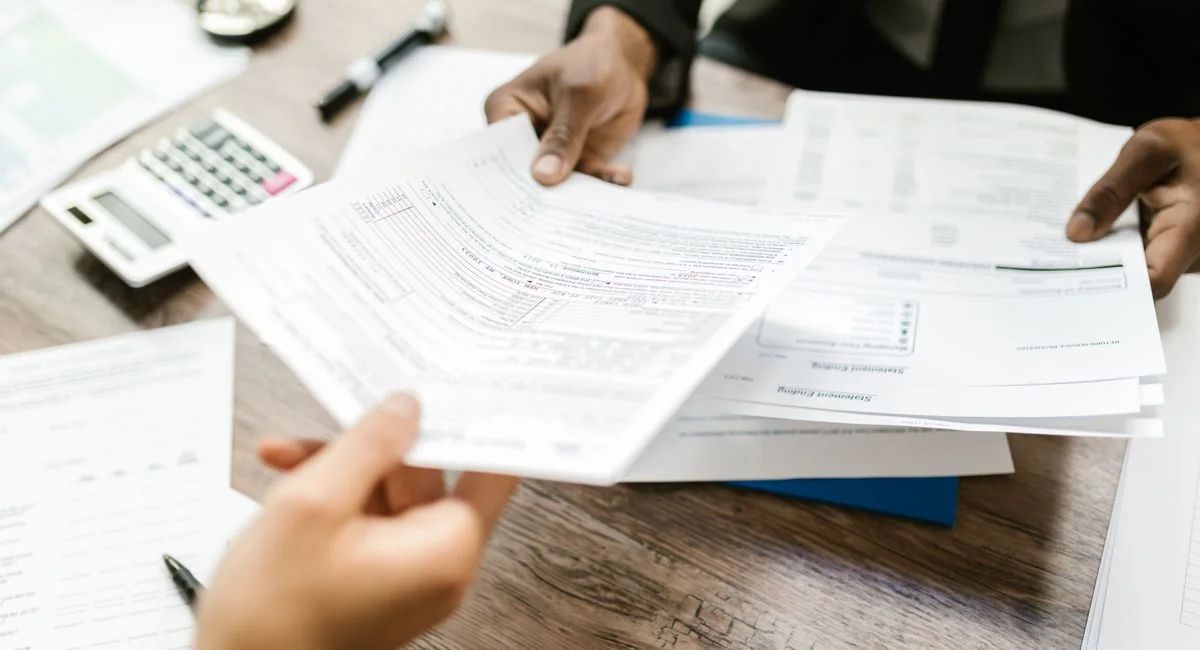 Two professionals exchanging documents in an office setting, focusing on paperwork and data analysis.