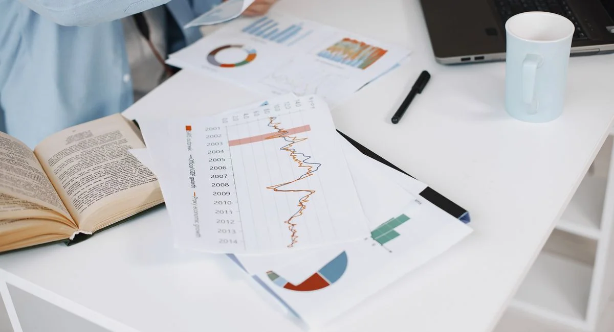 Office workspace with data charts, book, and laptop on a white desk.