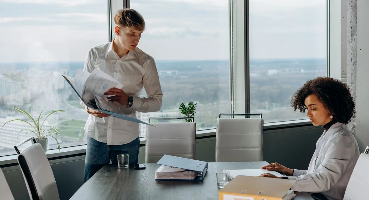 Business professionals reviewing documents in a bright, modern office setting with a city view.