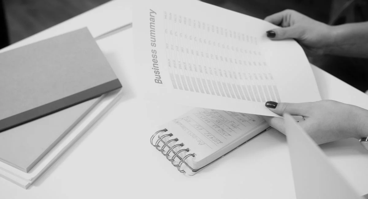 Black and white image of a businesswoman reviewing a business summary on paper.